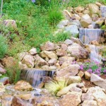Backyard Design Waterfall Pretty Backyard Design Including Stone Waterfall Flowing From Up To Down Area With Some Plants And Flowers On Ground Garden  Backyard Garden Waterfalls As Beautiful Garden Landscaping 